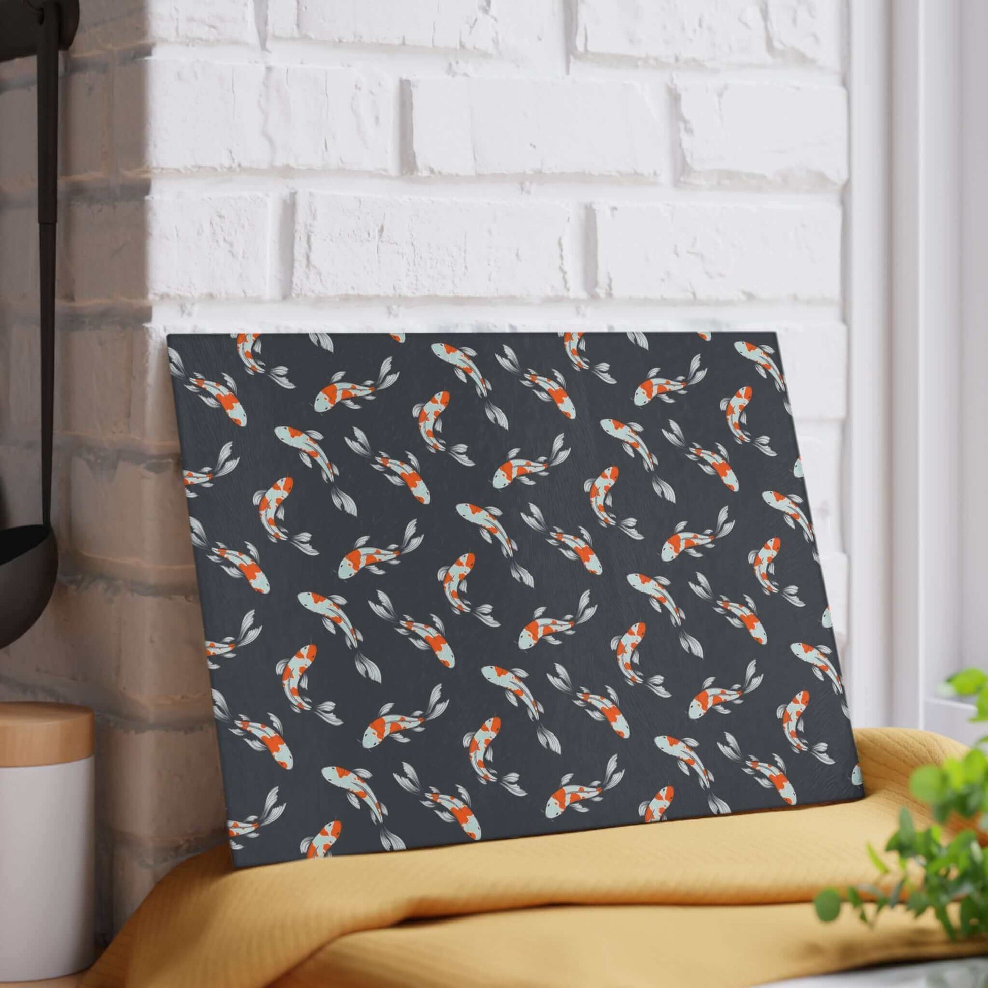 Carp and Koi Fish Glass Cutting Board with vibrant fish design displayed against a white brick wall.