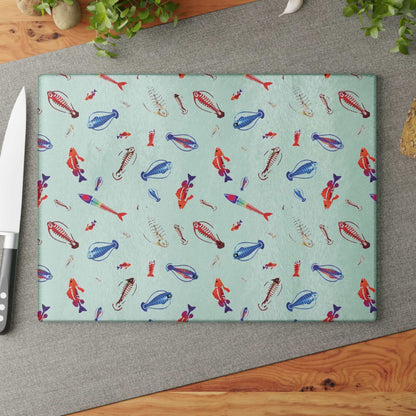 Deep Sea Skeleton Fish Glass Cutting Board with colorful fish design on a kitchen counter with a knife and greenery.