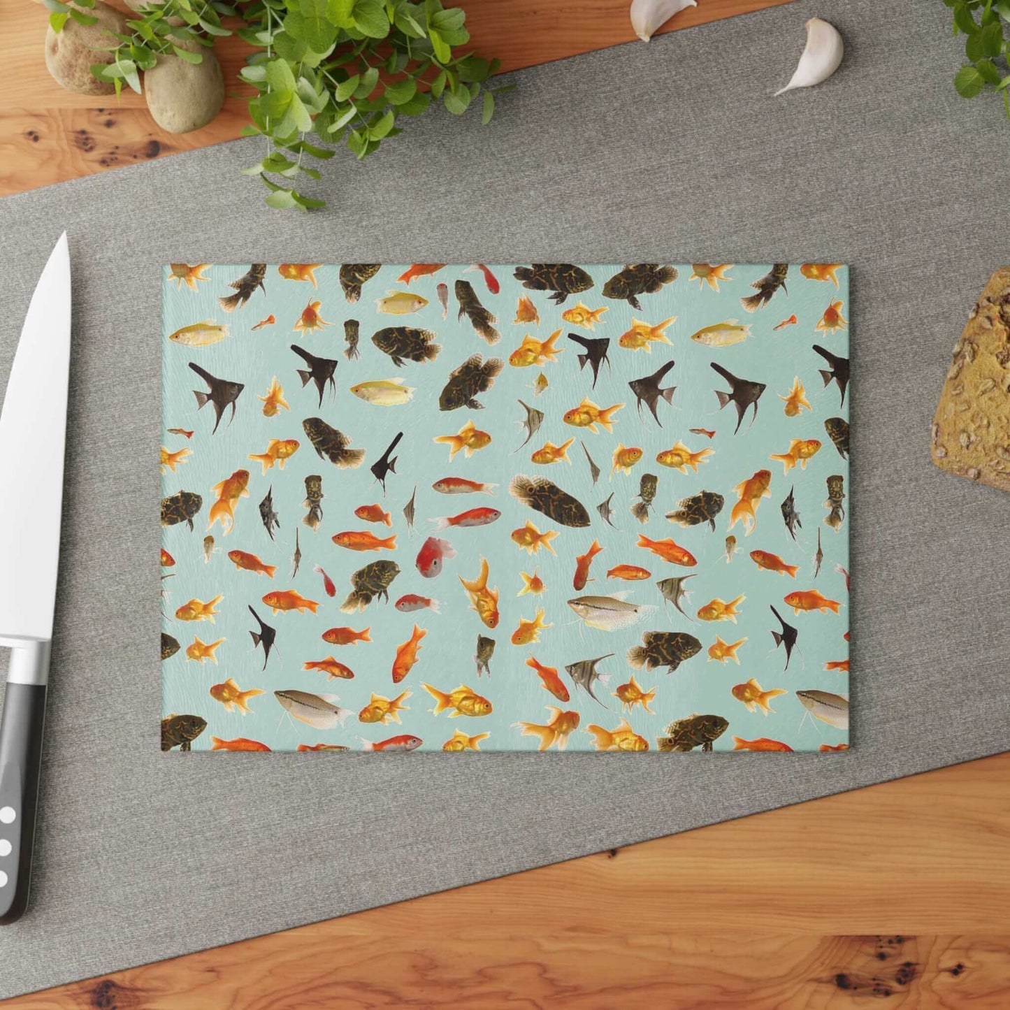 Vibrant aquarium fish design glass cutting board on a kitchen counter with a knife and herbs.