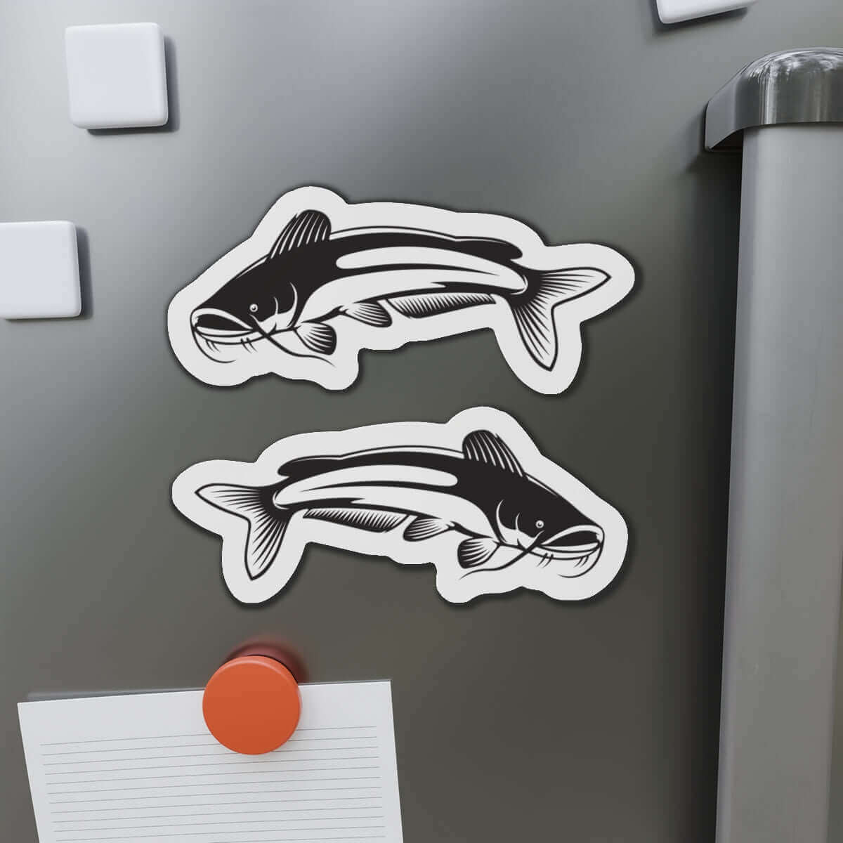 Two catfish-shaped magnets on a gray refrigerator door, adding a natural flair to the magnetic surface.