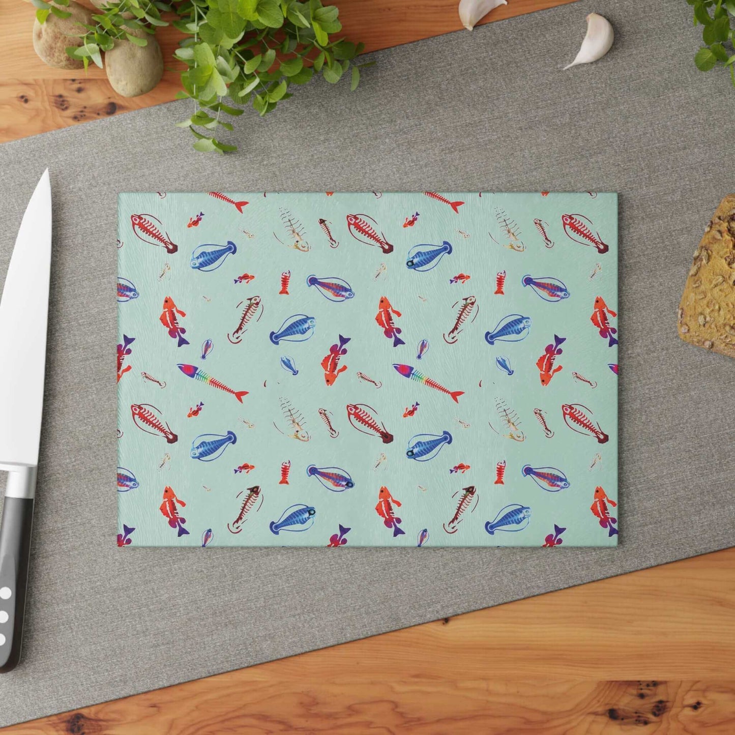 Deep Sea Skeleton Fish glass cutting board with vibrant fish design on kitchen counter with knife and greenery.