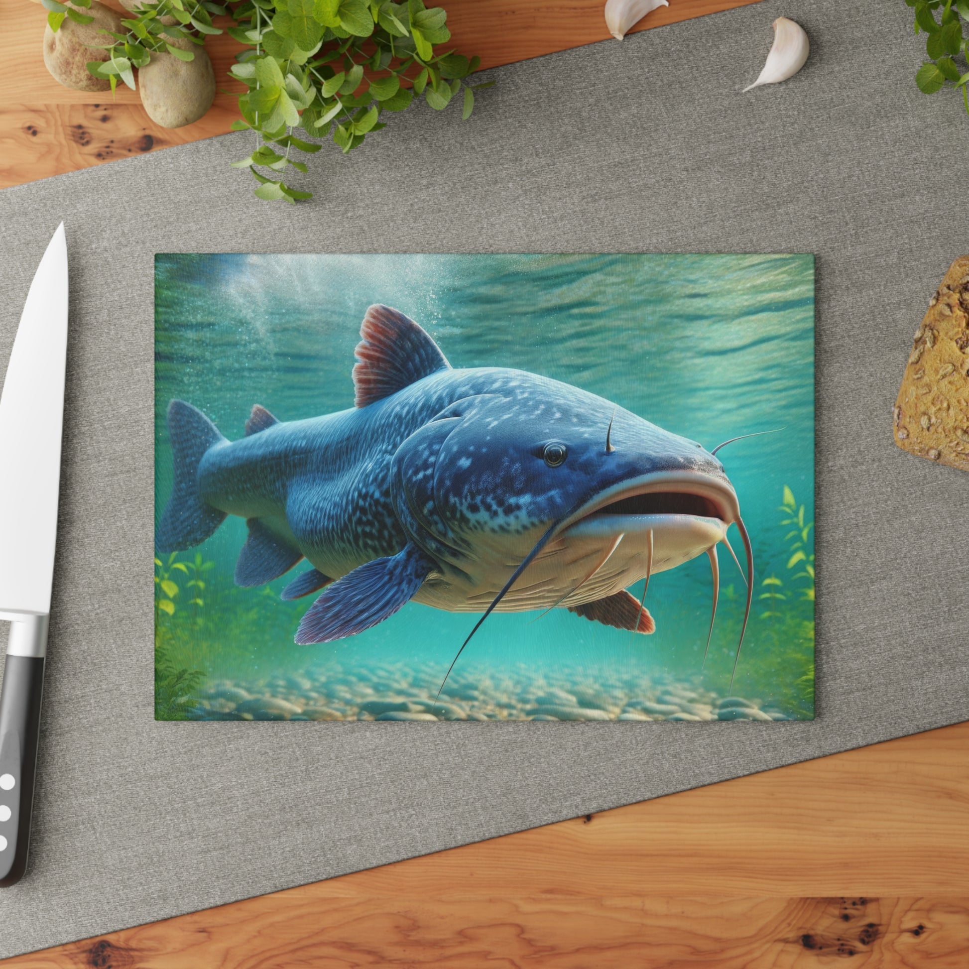 Catfish glass cutting board with vibrant fish design on kitchen counter with knife and herbs.