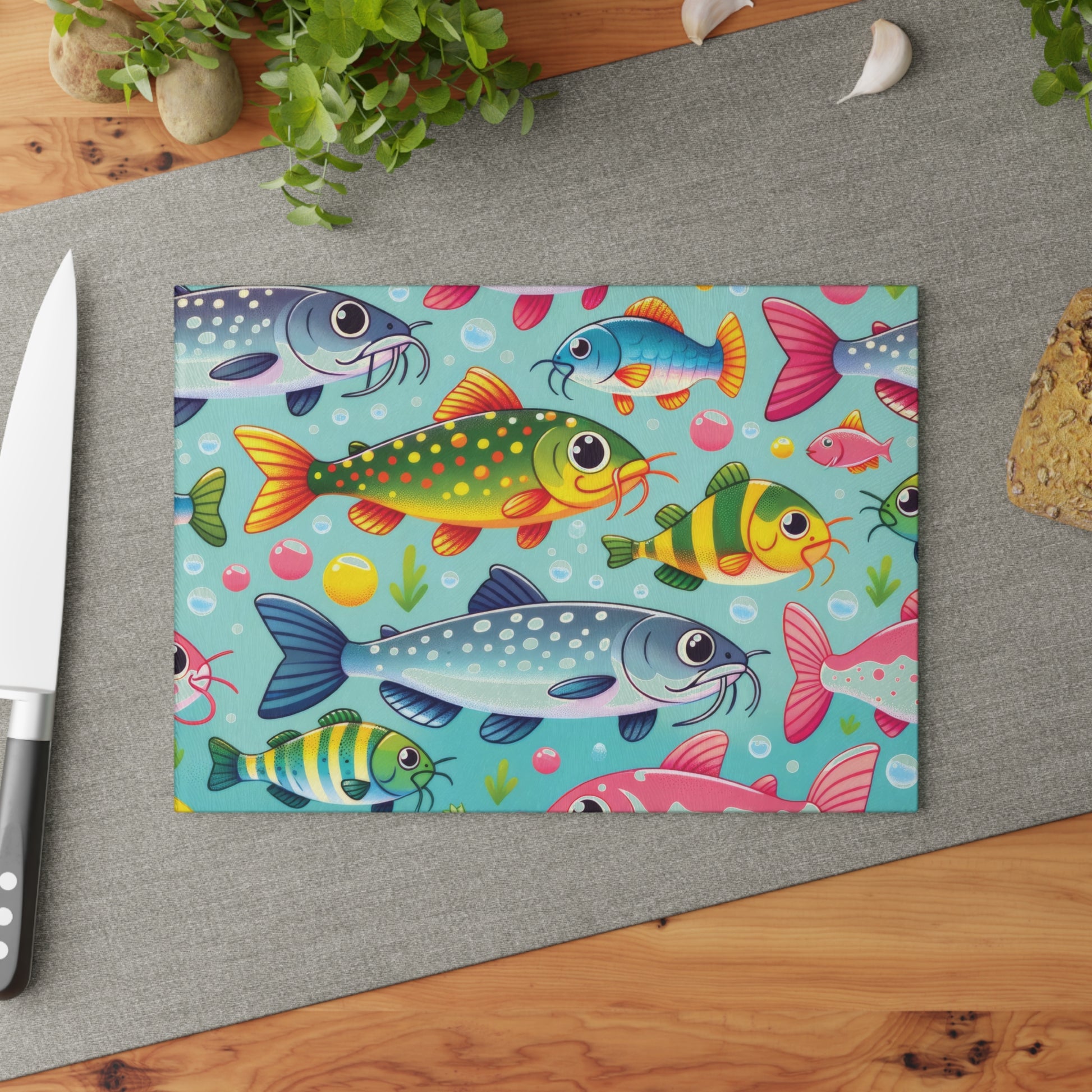 Colorful fish-themed glass cutting board on kitchen counter with knife and herbs