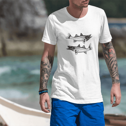 Man wearing white Snook T-Shirt with black and white fish design, perfect for fishing enthusiasts, on a beach.