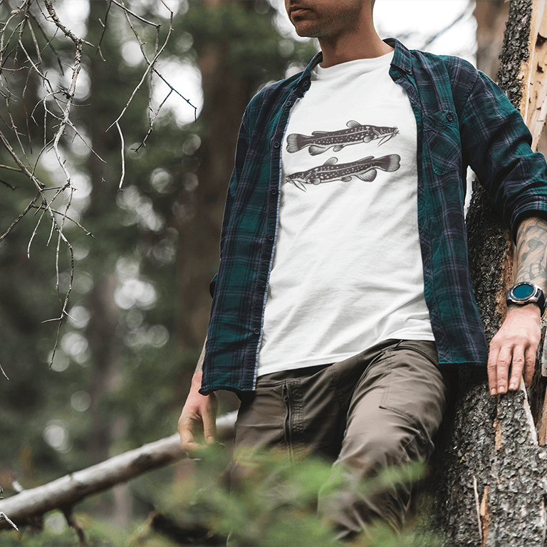 Man wearing Flathead Catfish T-shirt while leaning against a tree in a forest