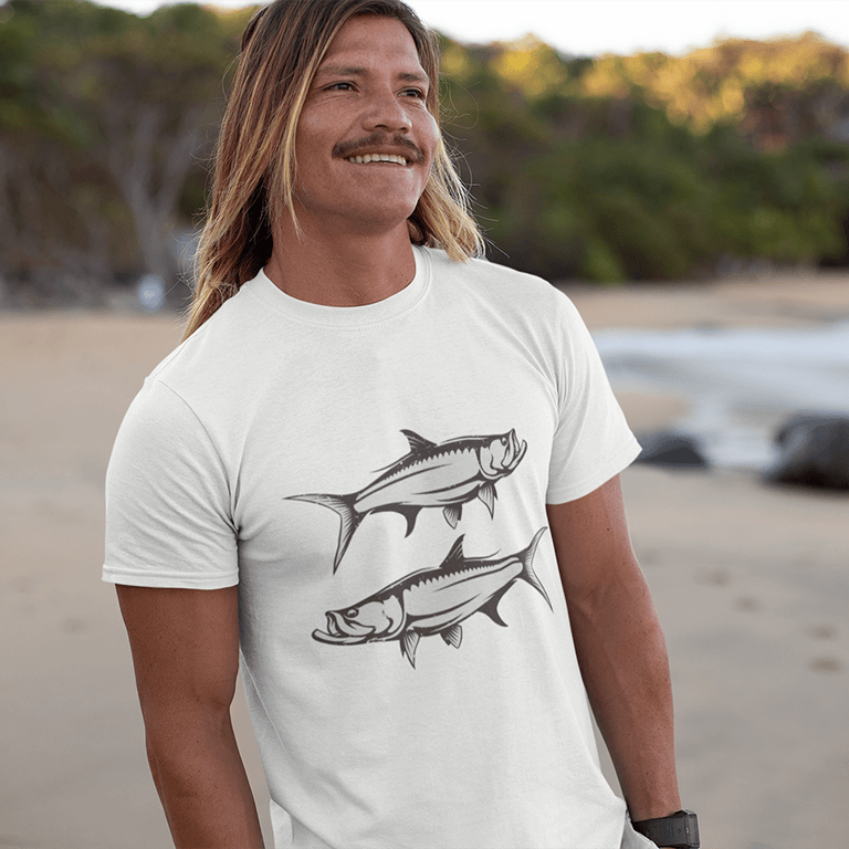 Man wearing white Tarpon T-Shirt with black and white fish design, standing on a beach.